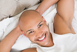 Close up of a smiling young bald man resting in bed