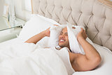 Sleepy man covering ears with pillow in bed