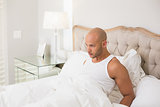 Thoughtful young bald man sitting in bed