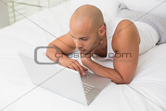 Casual bald man using laptop in bed