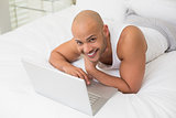 Smiling bald man using laptop in bed