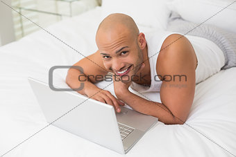 Smiling bald man using laptop in bed