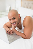 Smiling casual bald man using laptop in bed