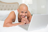 Smiling casual bald man using laptop in bed