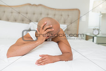Sleepy bald man looking at alarm clock in bed