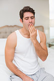 Young man yawning in bed at home
