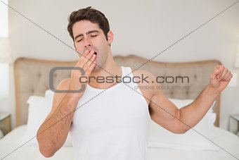 Young man waking up in bed and stretching arms