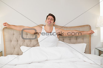 Young smiling man stretching arms in bed
