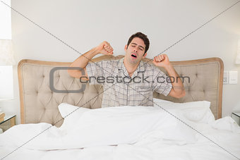 Young man waking up in bed and stretching his arms