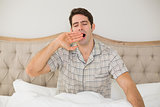 Young man sitting and yawning in bed