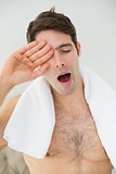 Shirtless man yawning as he rubs his eye
