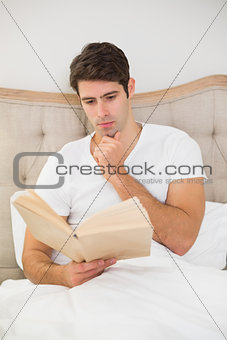 Relaxed man reading book in bed