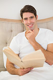 Portrait of relaxed young man reading book in bed