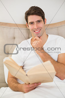 Portrait of relaxed young man reading book in bed