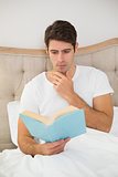 Relaxed young man reading book in bed