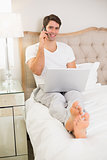 Casual man using cellphone and laptop in bed