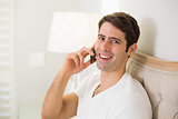 Casual smiling man using cellphone in bed
