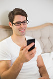 Casual smiling young man text messaging in bed