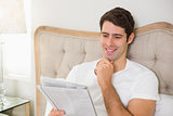 Casual smiling man reading newspaper in bed