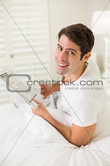Portrait of smiling casual man reading newspaper in bed
