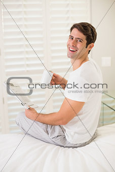 Cheerful man with coffee cup reading newspaper in bed