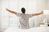 Rear view of a man stretching his arms in bed