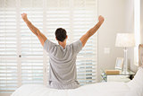 Rear view of man stretching his arms in bed