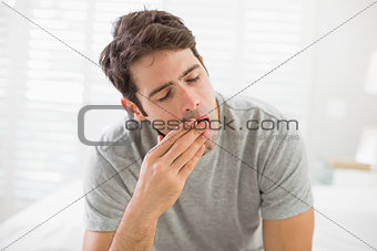 Sleepy young man sitting and yawning in bed