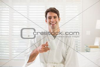 Smiling man in bathrobe drinking coffee in bedroom