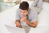 Casual young man using laptop in bed