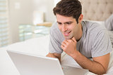 Casual smiling man using laptop in bed