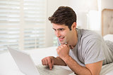 Casual smiling young man using laptop in bed