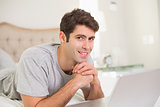 Portrait of casual smiling man using laptop in bed