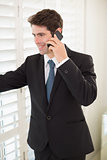 Smiling businessman peeking through blinds while on call