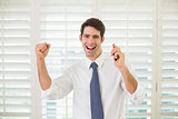 Cheerful businessman with mobile phone clenching fist in office