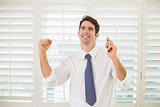 Businessman with mobile phone clenching fist in office