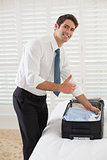 Smiling businessman unpacking luggage at a hotel bedroom