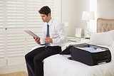 Businessman with coffee cup and newspaper by luggage at hotel room