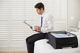 Businessman with coffee cup and newspaper by luggage at hotel room