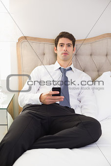 Serious well dressed man with cellphone sitting in bed