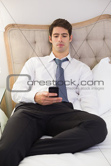 Serious well dressed man text messaging in bed