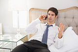 Serious well dressed man using mobile phone in bed