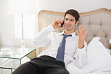 Smiling well dressed man using mobile phone in bed