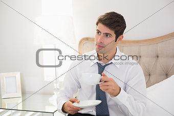 Serious well dressed man with a cup of tea in bed