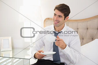 Smiling well dressed man with a cup of tea in bed