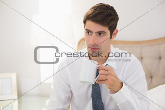 Serious well dressed man drinking coffee in bed