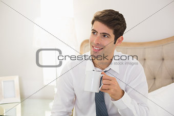 Smiling well dressed man drinking coffee in bed