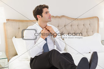 Elegant young businessman adjusting tie in bed