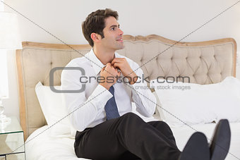 Smiling businessman adjusting tie in bed