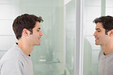 Side view of a young man smiling at self in bathroom mirror